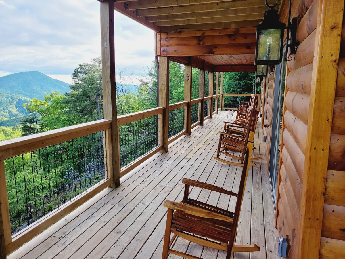 This exterior image showcases a portion of the wooden deck with classic rocking chairs facing out toward a dramatic mountain view. The railing and beams frame the distant landscape, inviting relaxation and conversation while soaking in the beauty of the Smokies.