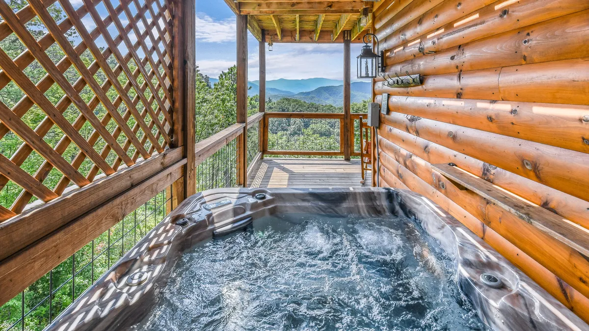 A tranquil hot tub sits on a spacious wooden deck overlooking distant mountains. Steam rises from the bubbling water, and the deck’s sturdy railing frames spectacular views, perfect for unwinding after a day of adventure or stargazing at night.