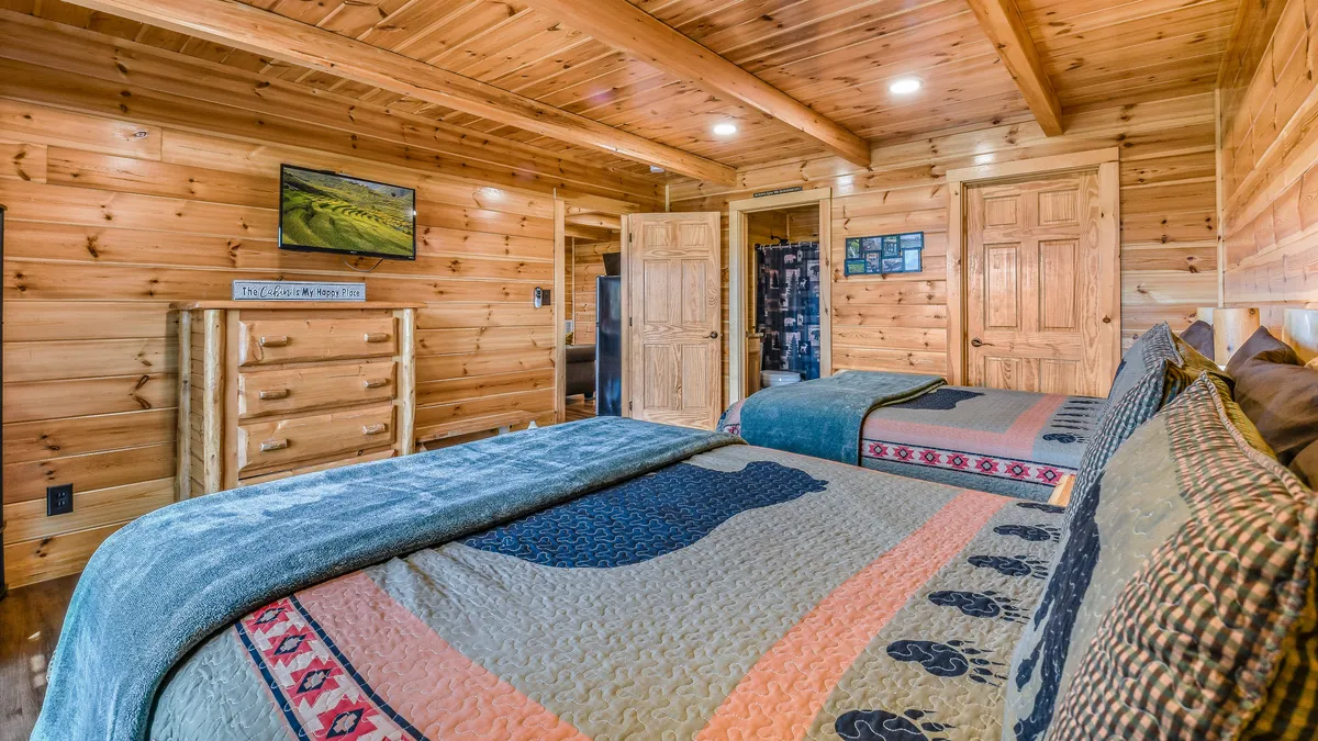 A spacious guest suite featuring two beds with colorful, decorative quilts, a wooden dresser, and warm lighting. The room evokes the comfort of a rustic cabin and offers ample space for families or friends to unwind together.