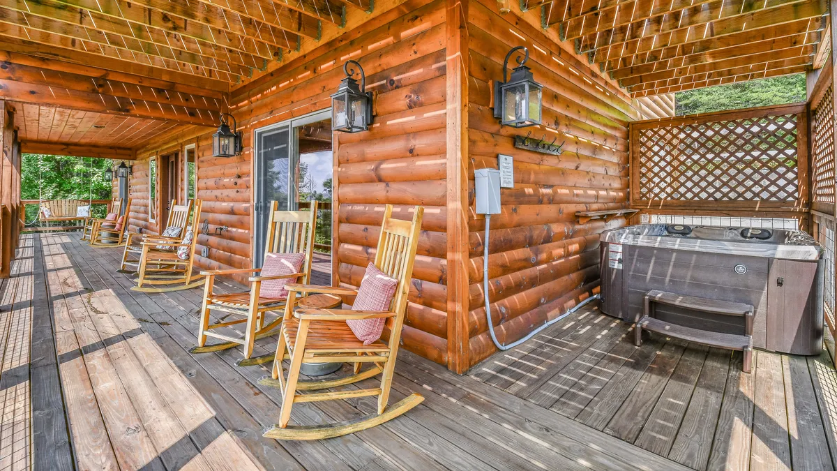 A wide shot of the deck that features both rocking chairs and a hot tub, with lanterns adding a cozy touch. The mountain view stretches beyond, while the setup encourages group relaxation and memory-making in a single, inviting space.