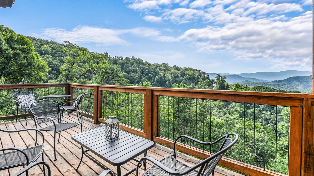 A wooden deck furnished with outdoor seating and a table with a lantern, all overlooking a sweeping mountain view. The tranquil setting is ideal for social gatherings, stargazing, or relaxing after a day at local attractions.