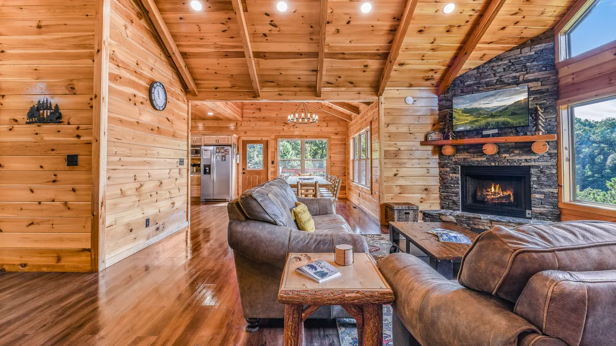 A warm and inviting living area with a stone fireplace, plush seating, wooden beams, and expansive windows offering breathtaking mountain vistas. The space is perfect for relaxing by the fire, reading, or enjoying the view with family and friends.