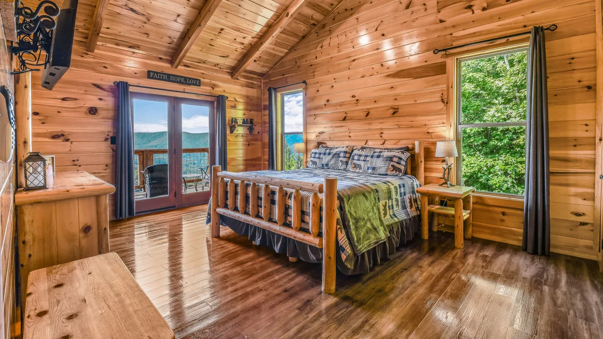 This image showcases a log bed set against wooden walls with large windows framing scenic views. Decorative lighting, a bedside lantern, and a serene ambiance create a tranquil retreat ideal for relaxation and quiet reflection.
