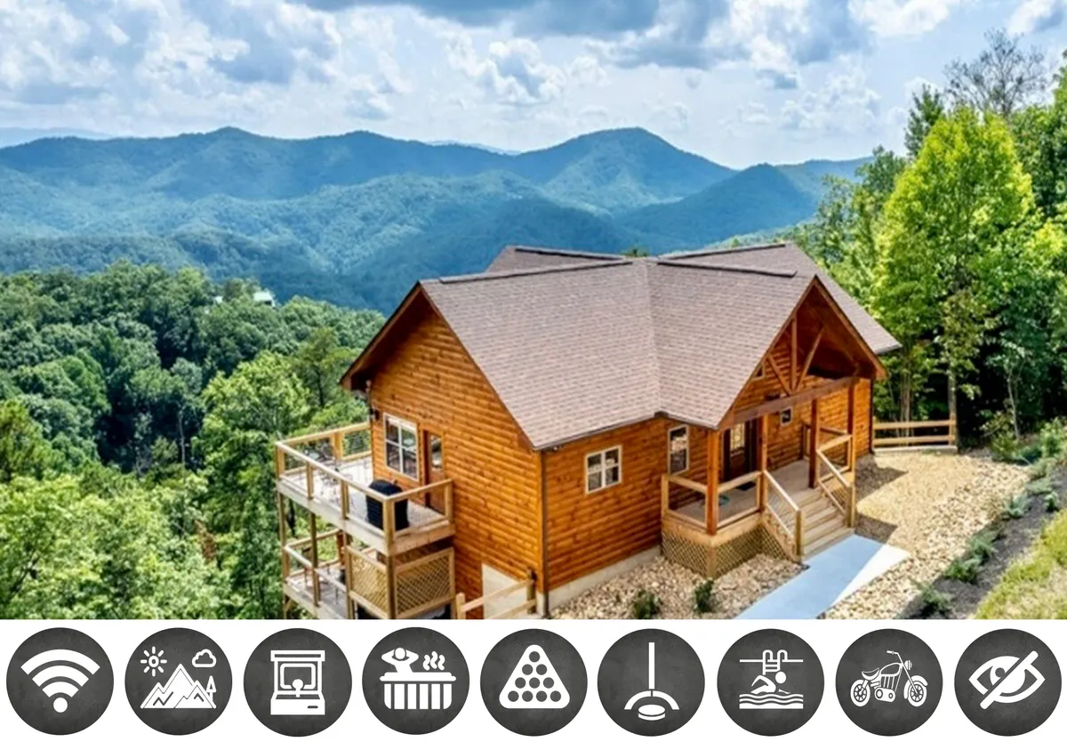 The image showcases a stunning, newly-built log cabin nestled in lush greenery, perched atop a ridge with sweeping views of the Smoky Mountains. A spacious wooden deck wraps around the cabin, perfect for relaxing, dining, or taking in sunsets. The tranquil setting exudes peace and invites guests to unwind and connect with nature.