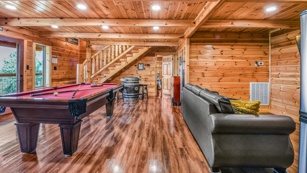 This image captures a cozy corner of the game room, featuring a pool table, a plush sofa for relaxing, a wooden staircase, and a barrel table. The setup encourages both energetic play and comfortable lounging, echoing the section's themes of relaxation and fun.